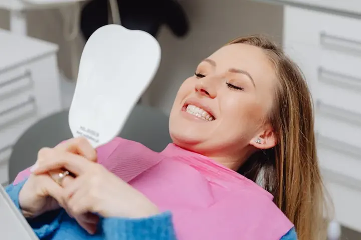 Smiling woman in a dental chair admiring her new smile in a mirror